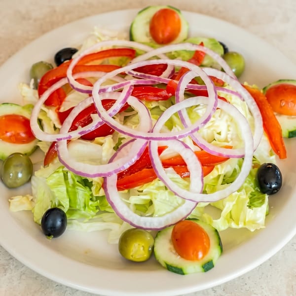 A fresh garden salad with lettuce, red onions, bell peppers, cucumbers, and olives on a white plate.