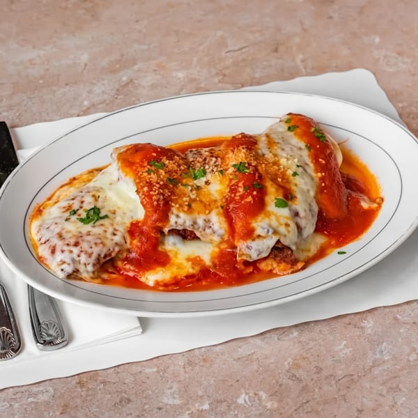 Chicken parmesan with melted mozzarella, red sauce, and parsley on a white oval plate with silverware.