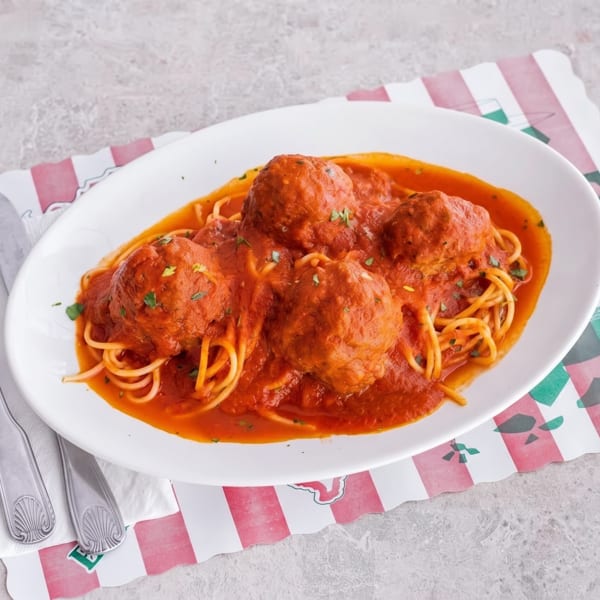 Spaghetti and meatballs in red sauce, garnished with herbs, on a white plate with silverware.