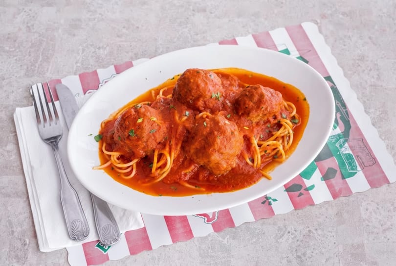 Spaghetti and meatballs in red sauce, garnished with herbs, on a white plate with silverware.
