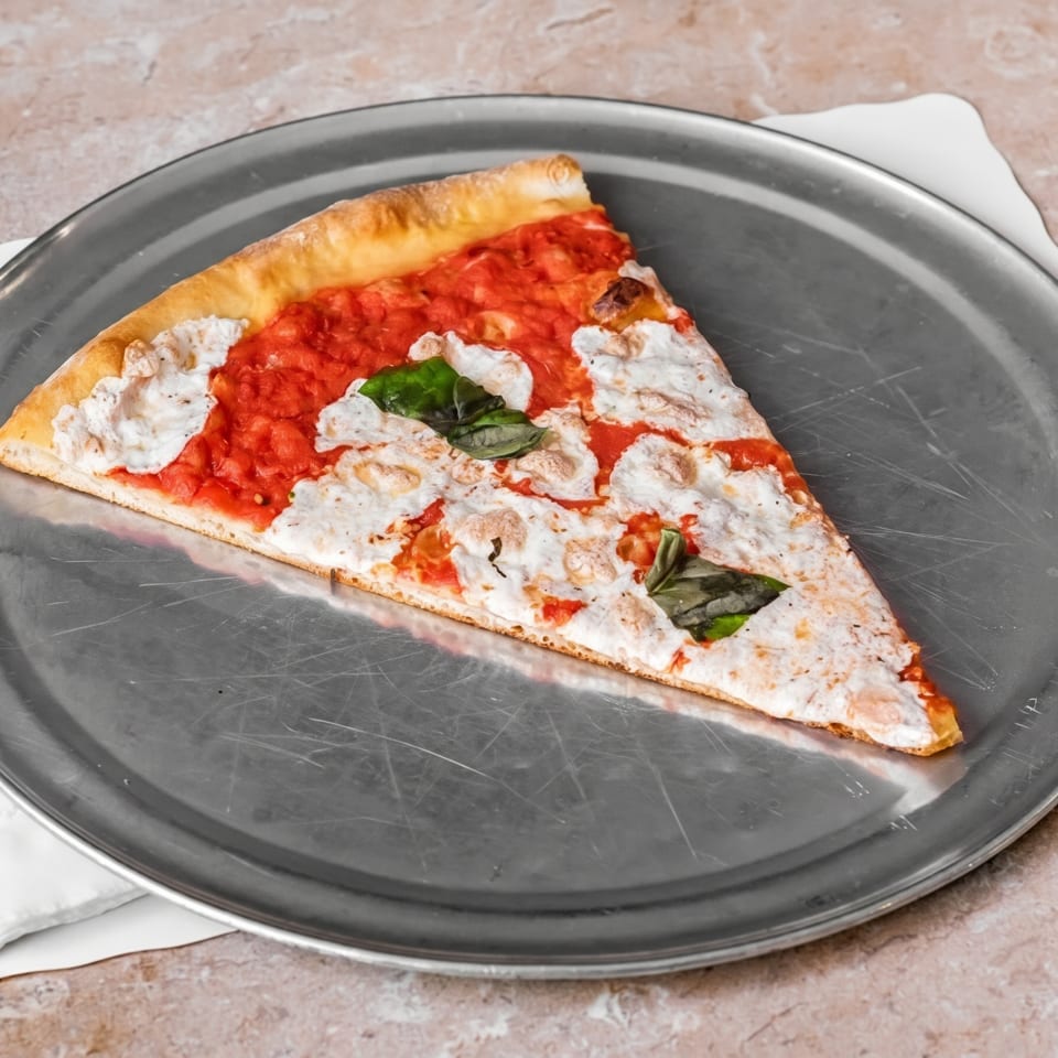 A single slice of pizza with red sauce, white cheese, and basil on a metal tray.