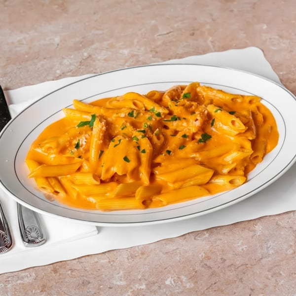 Penne pasta in a creamy orange sauce, garnished with parsley and parmesan cheese.