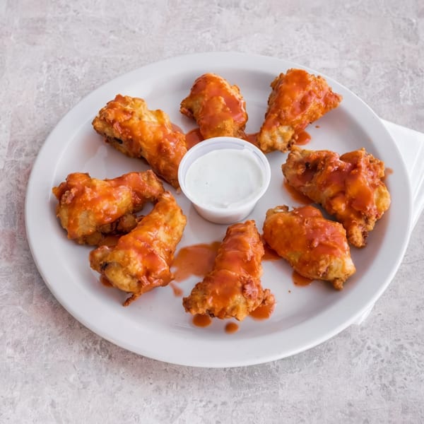 A white plate holds eight buffalo chicken wings with a side of ranch dressing.